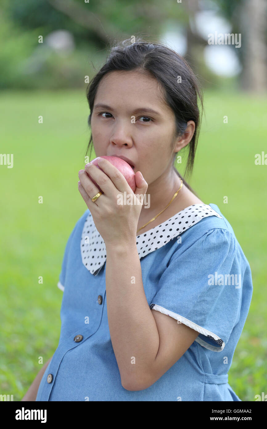 Asiatische schwangere Frauen, die mit der Hand fangen Apfel essen im öffentlichen Park. Stockfoto
