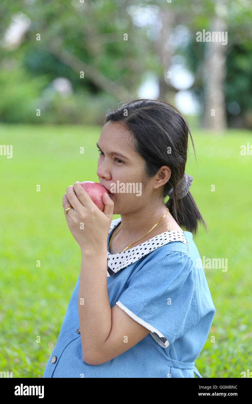 Asiatische schwangere Frauen, die mit der Hand fangen Apfel essen im öffentlichen Park. Stockfoto