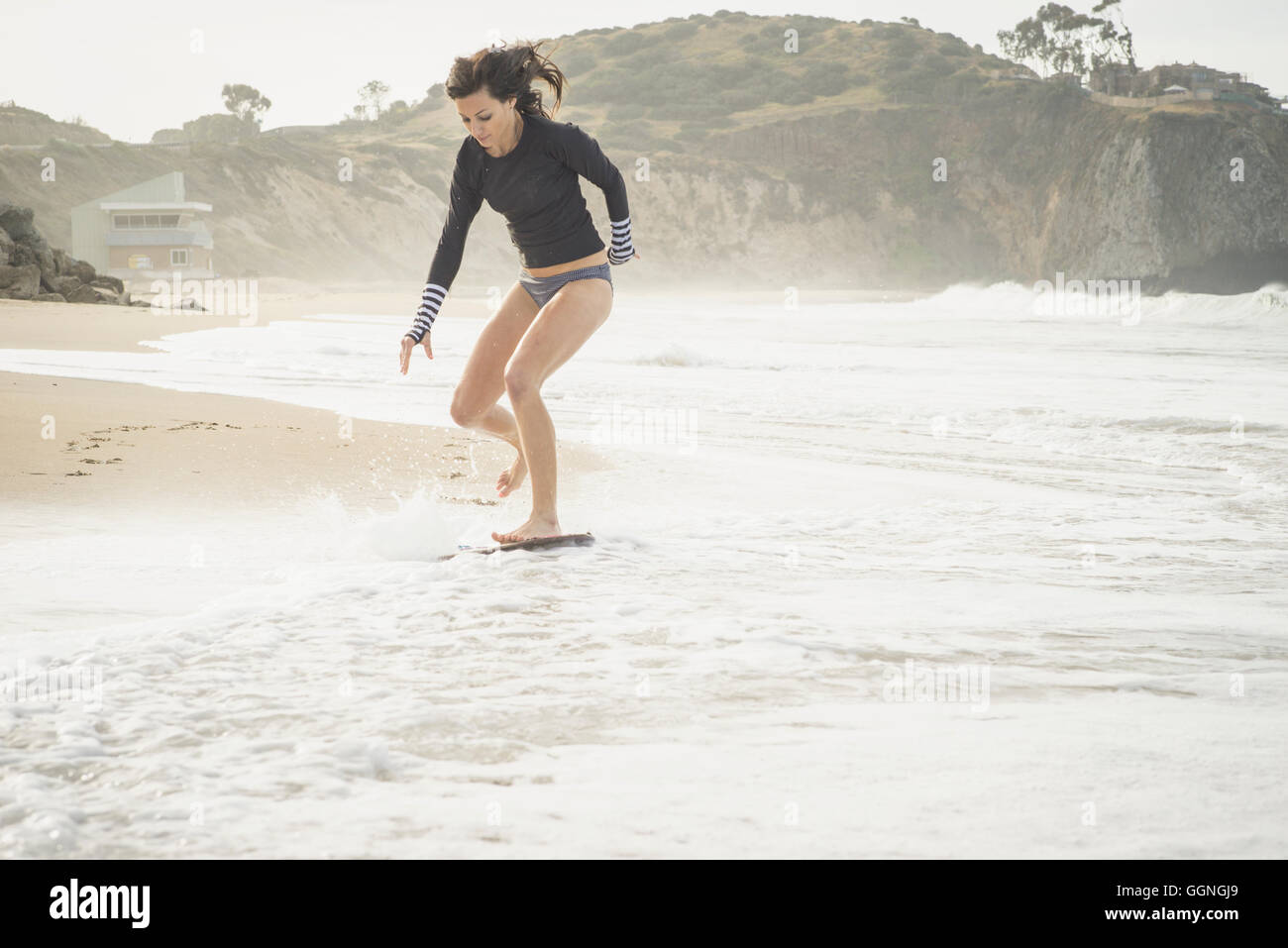 Kaukasische Frau Skimboard am Strand Reiten Stockfoto