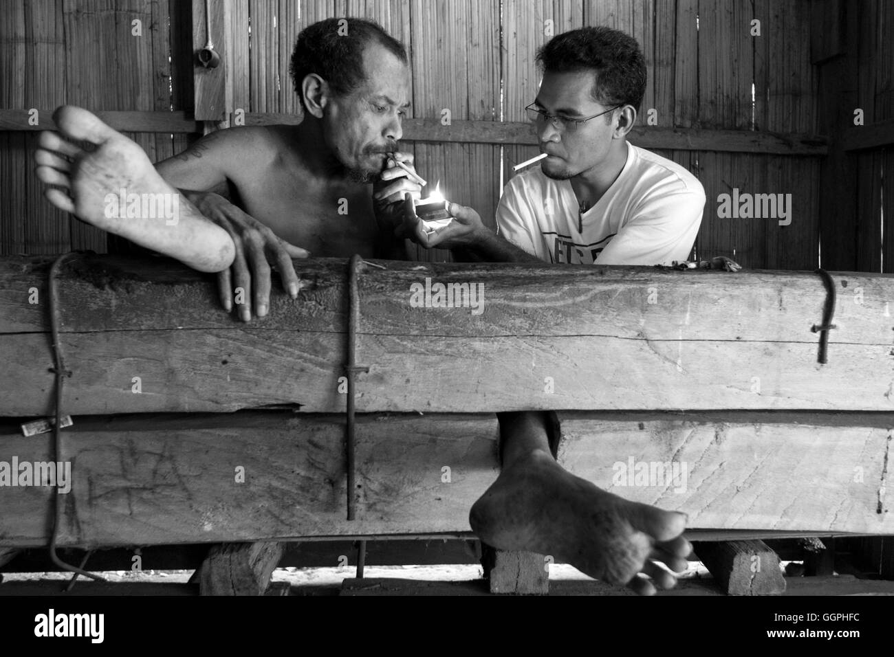Vater Aventinus Saur zündet sich eine Zigarette für Deo Gracias Kolobanus Abri. Abri ist ein psychisch kranker Mann, der zu einem Strahl in seiner Heimat seit 1997 gefesselt wurde. Die Familie der Abri sperrte ihn in Aktien nach begann er Angriff auf Nachbarn und Durchgangsverkehr. Vater Saur läuft eine Gruppe, die kümmert sich um und bringt Trost für die Opfer und Familien von psychisch leidenden. Laut Human Rights Watch gibt es mindestens 18.800 Menschen derzeit in Indonesien wegen Geisteskrankheit gefesselt wird. Familienmitglieder sagen Verwandten sind gefesselt oder angekettet, um sie daran zu hindern, Schaden sich selbst. Auch Stockfoto