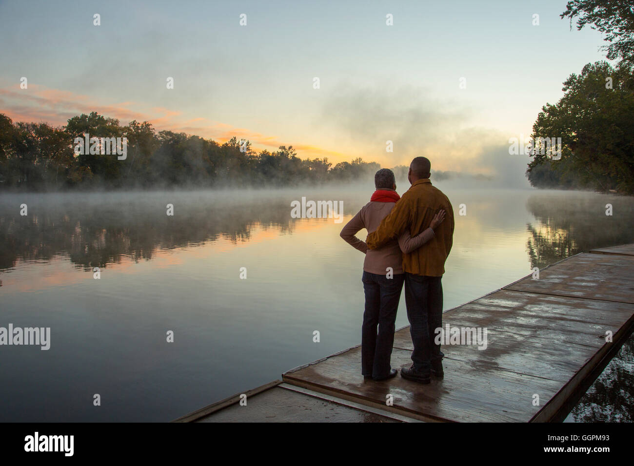 Älteres Ehepaar umarmt am nebligen River bei Sonnenaufgang Stockfoto