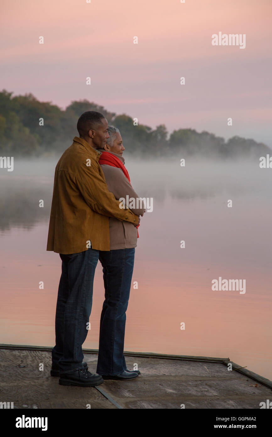 Älteres Ehepaar umarmt am nebligen River bei Sonnenaufgang Stockfoto