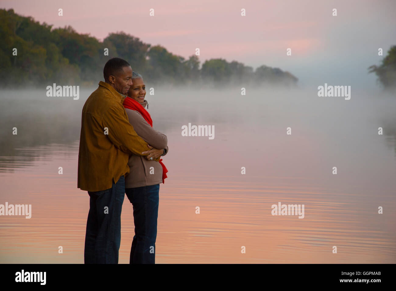Älteres Ehepaar umarmt am nebligen River bei Sonnenaufgang Stockfoto