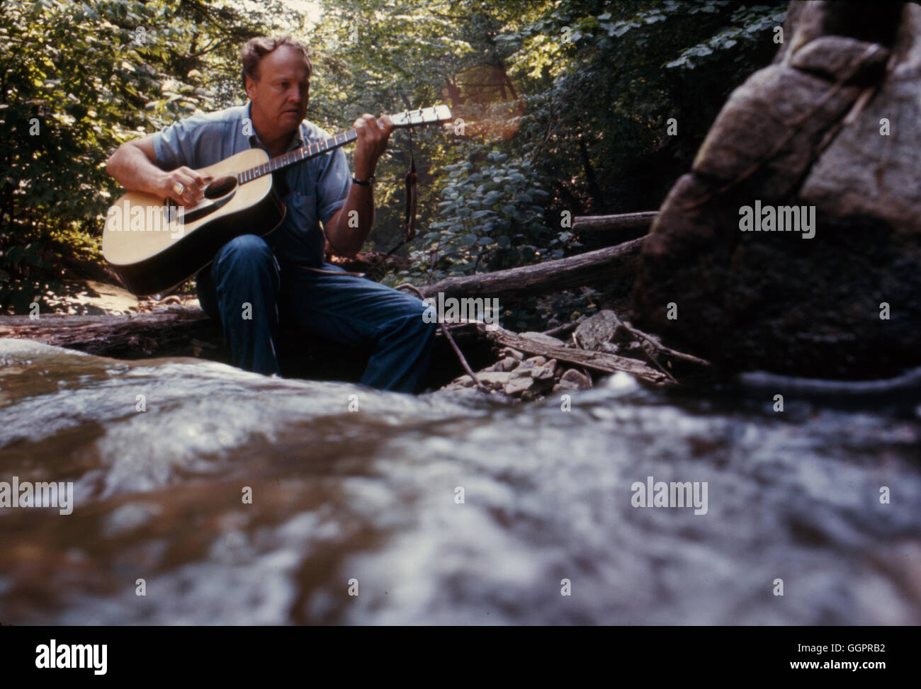 Autor James Dickey, am besten bekannt für seine neuartige Befreiung, Gitarre zu spielen, neben einem Bach, 23. Juni 1969 Stockfoto