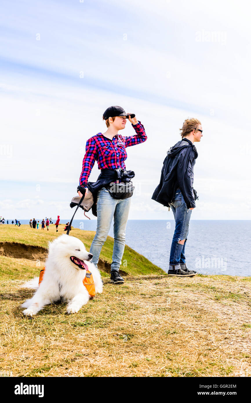 Kaseberga, Schweden - 1. August 2016: Echte Menschen im Alltag. Junge Erwachsene stehen auf windigen Hügel mit weißen Hund suchen Stockfoto