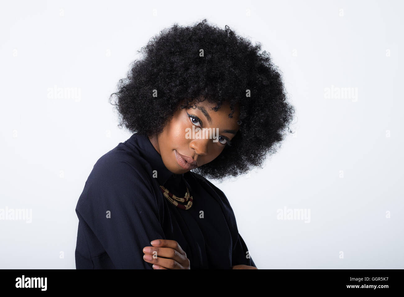 Ein junges afrokaribisches Modell sieht mit einem geneigten Kopf und einem rätselhaften Lächeln in die Kamera Stockfoto