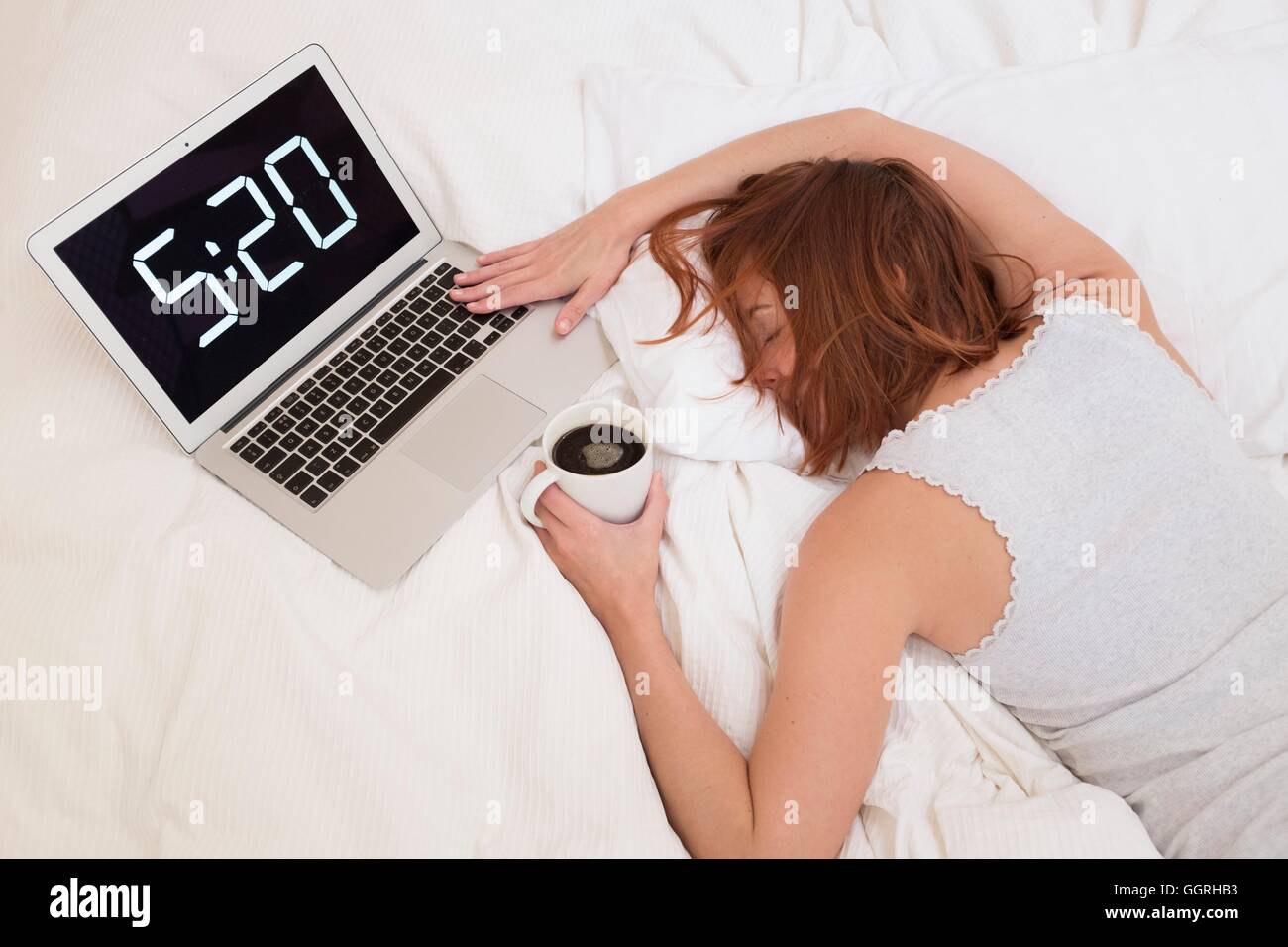 Erschöpfte Frau im Bett mit Laptop und Kaffee. Stockfoto