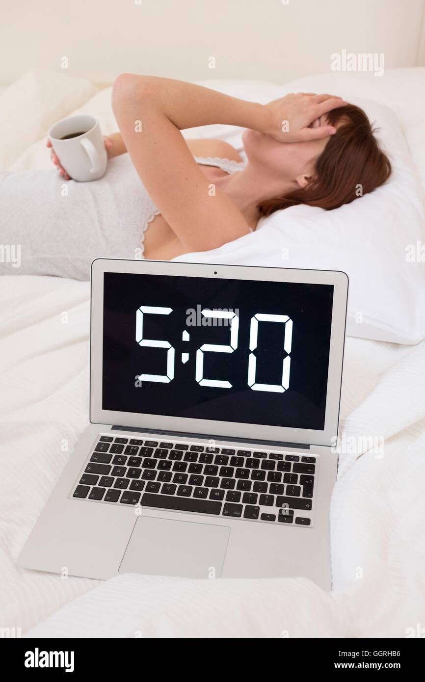 Erschöpfte Frau im Bett mit Laptop und Kaffee. Stockfoto