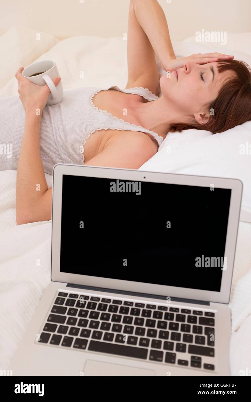 Erschöpfte Frau im Bett mit Laptop und schwarzen Kaffee. Stockfoto