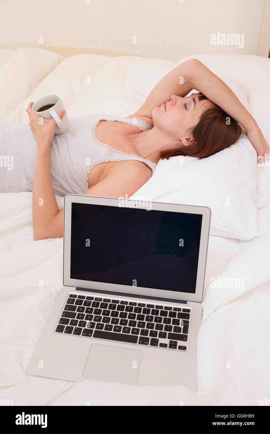Erschöpfte Frau im Bett mit Laptop und schwarzen Kaffee. Stockfoto