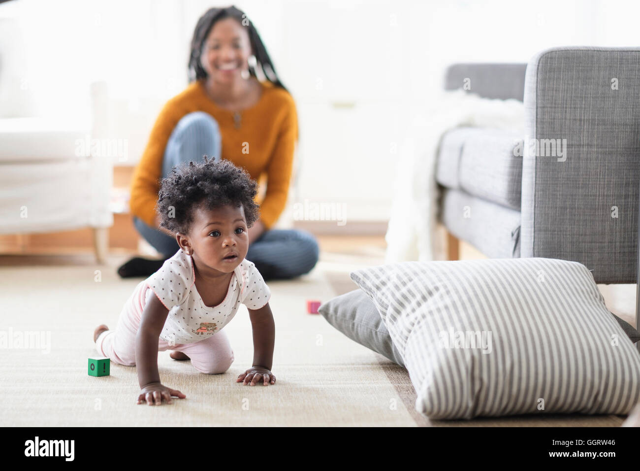 Schwarze Frau beobachten Baby Tochter Crawl auf Kissen Stockfoto