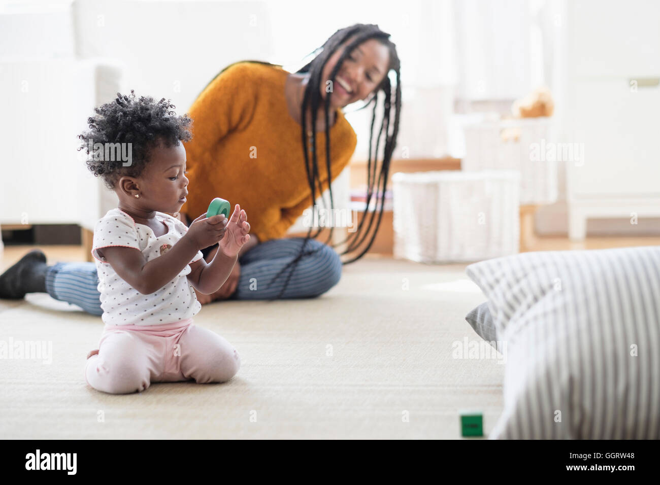 Schwarze Frau beobachten Baby Tochter spielen mit Spielzeug auf Teppich Stockfoto