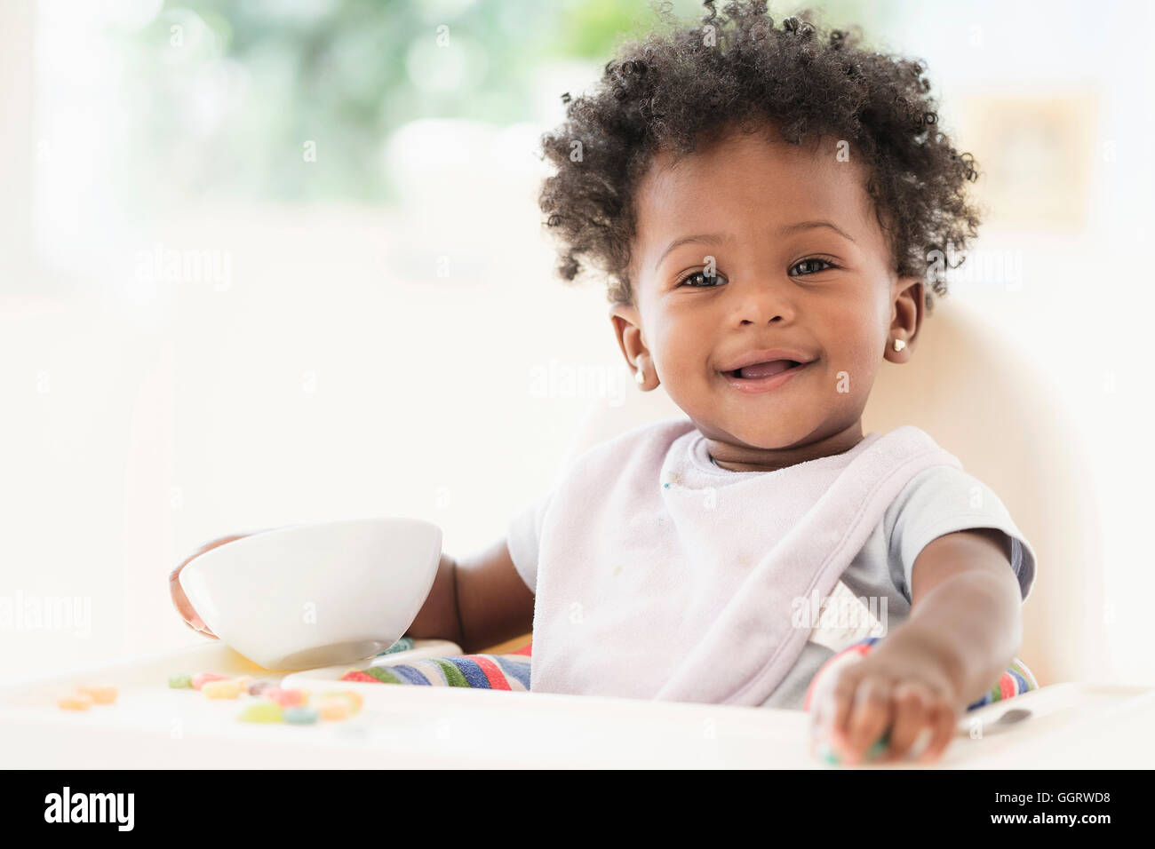 Lächelndes schwarzes Babymädchen essen Müsli aus Schüssel im Hochstuhl Stockfoto