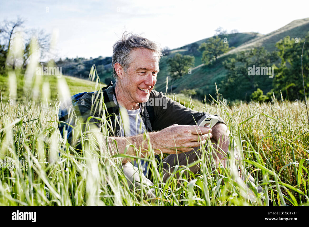 Kaukasische Wanderer sitzen in hohe Gräser mit Handy Stockfoto