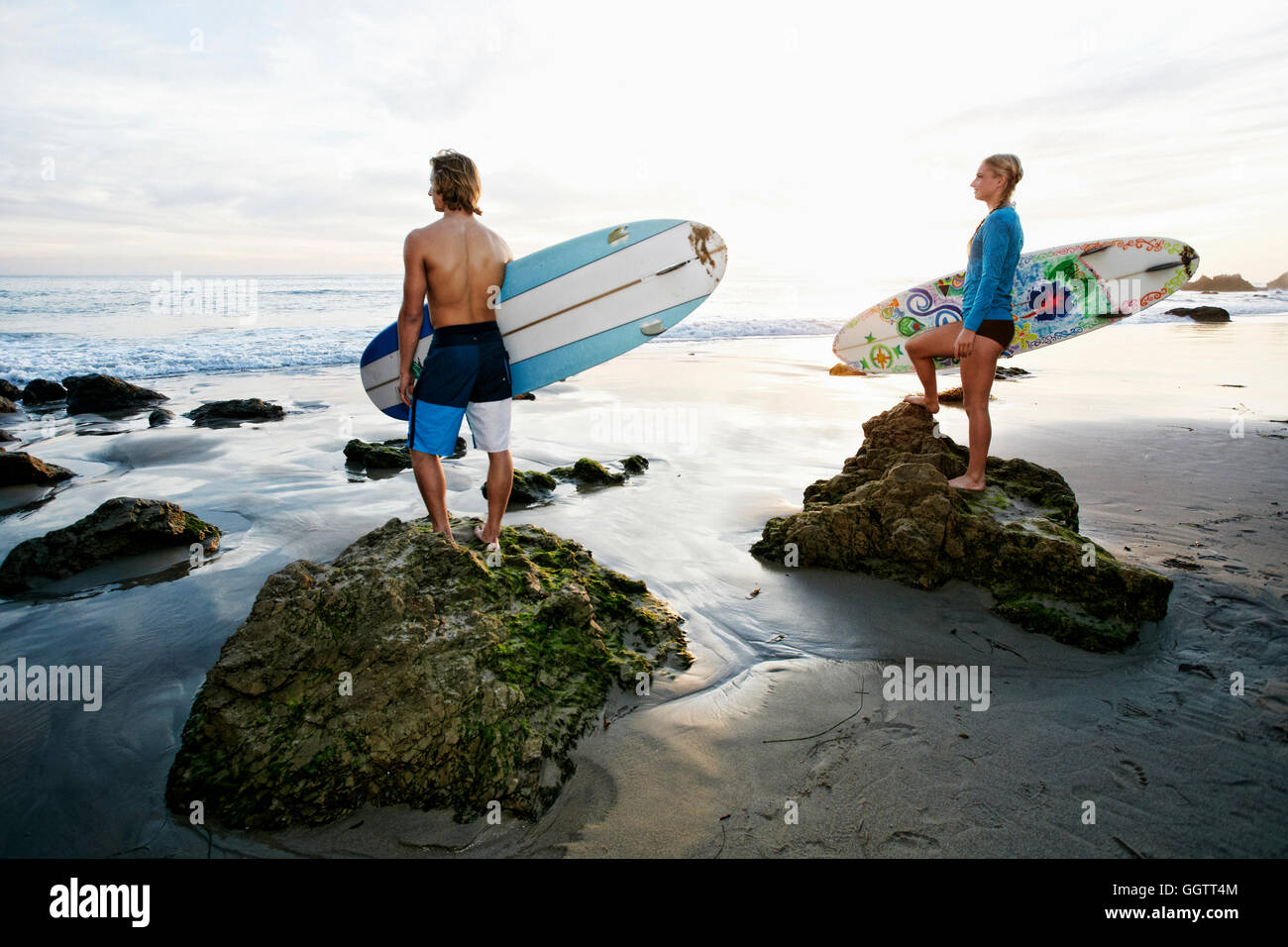 Kaukasische paar stehen auf Felsen tragen Surfbretter am Strand Stockfoto