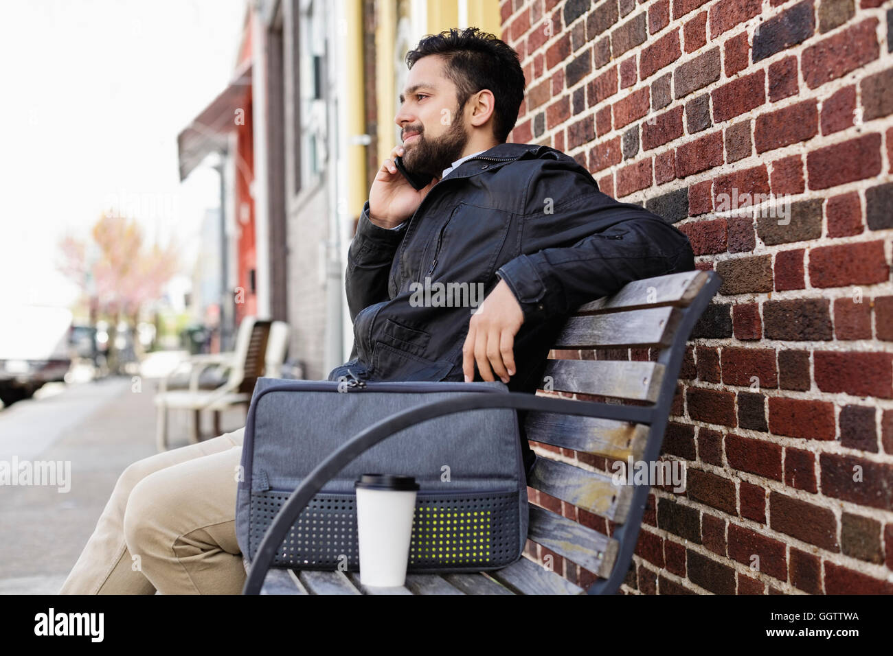 Hispanic Mann sitzt auf Stadt-Bank mit Handy Stockfoto