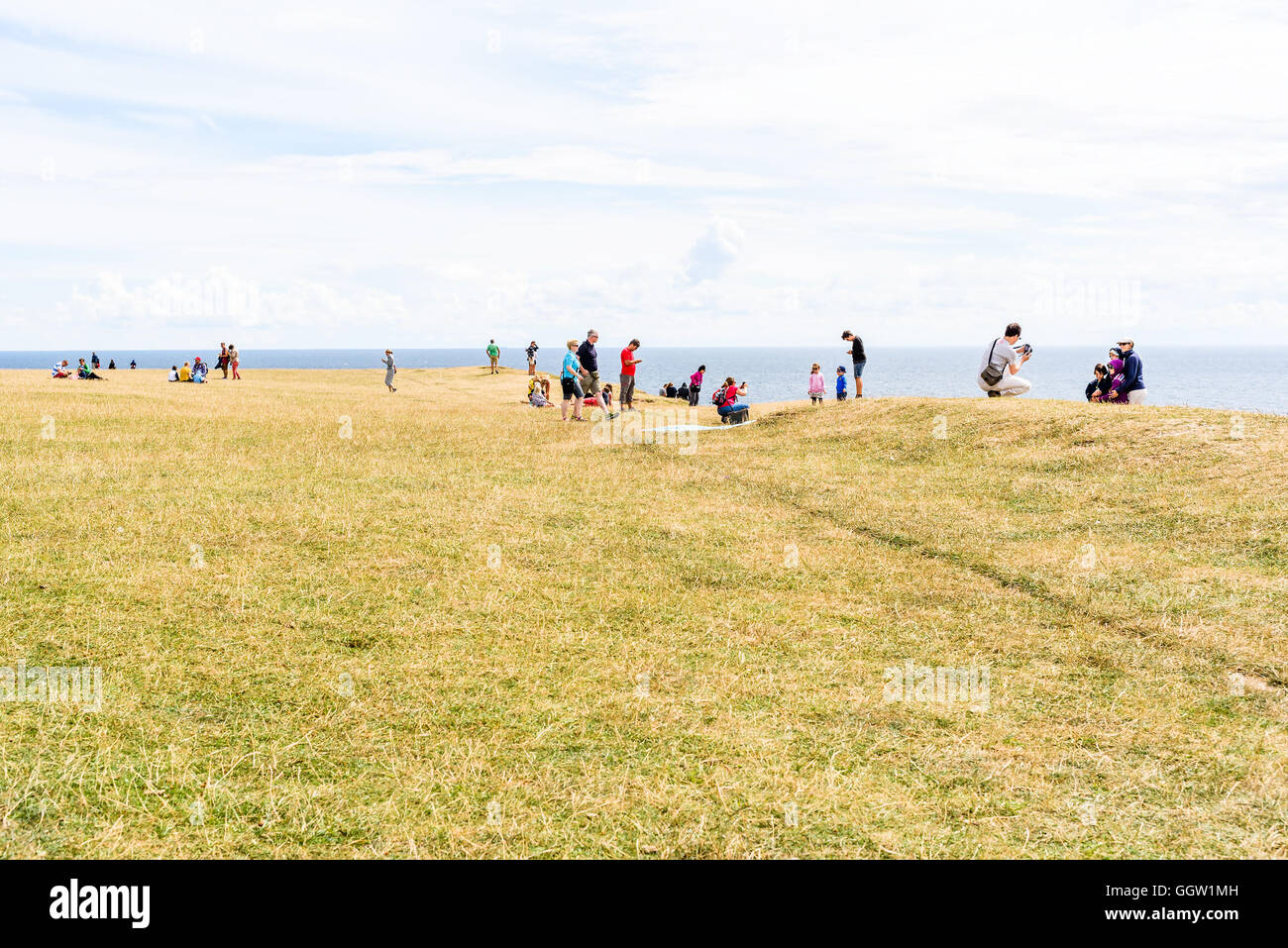 Kaseberga, Schweden - 1. August 2016: Touristen auf einer Wiese mit steilen Hänge hinunter zum Meer dahinter. Horizont über wate Stockfoto