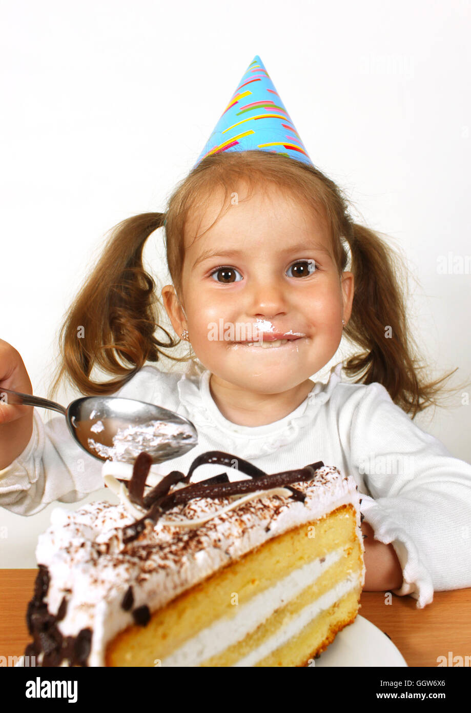 Porträt von verschmierten kleinen Mädchen mit Geburtstag Hut essen Kuchen Stockfoto