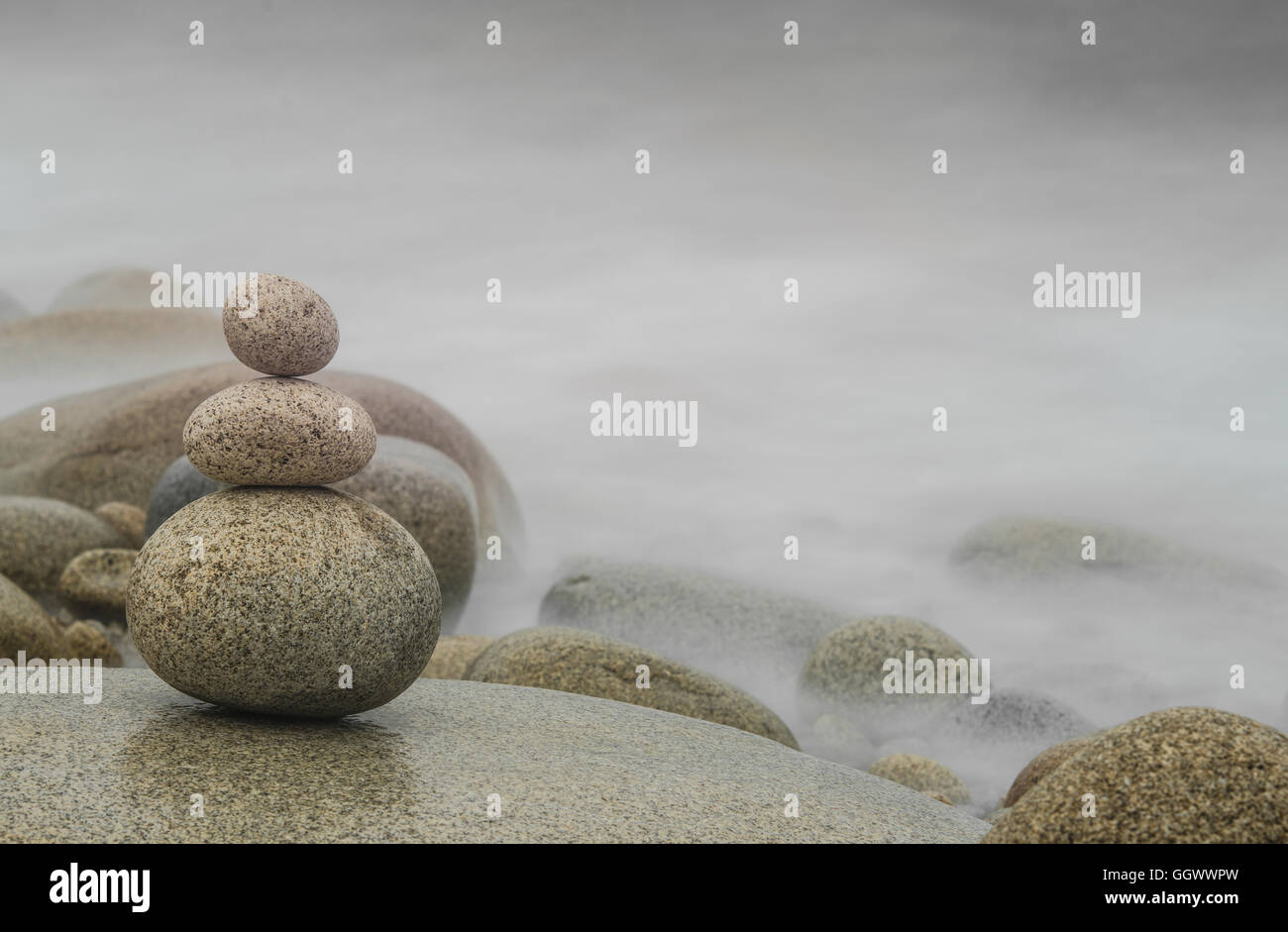 Drei Kieselsteine gestapelt im Vordergrund, nebligen Hintergrund mit freiem Speicherplatz für Text, Zen-Konzept, horizontales Bild. Stockfoto