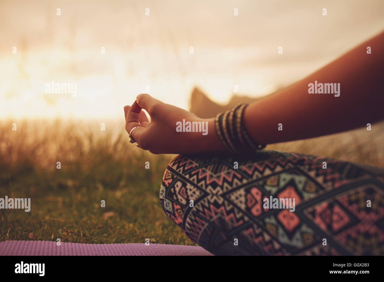 Nahaufnahme einer Frau in Lotusstellung, mit Fokus auf die Hände. Fitness-Frau, die während des Sonnenuntergangs im Freien meditiert. Stockfoto