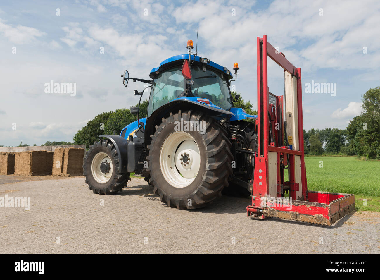 Blaue Traktor mit einem roten Ballen Hobel zum Abschneiden Silageballen Stockfoto