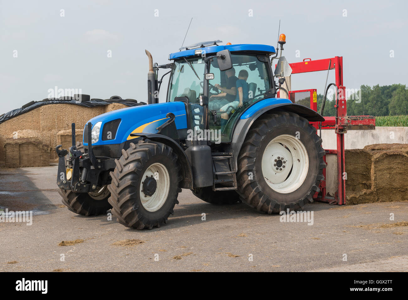 Blaue Traktor mit einem roten Ballen Hobel zum Abschneiden Silageballen Stockfoto