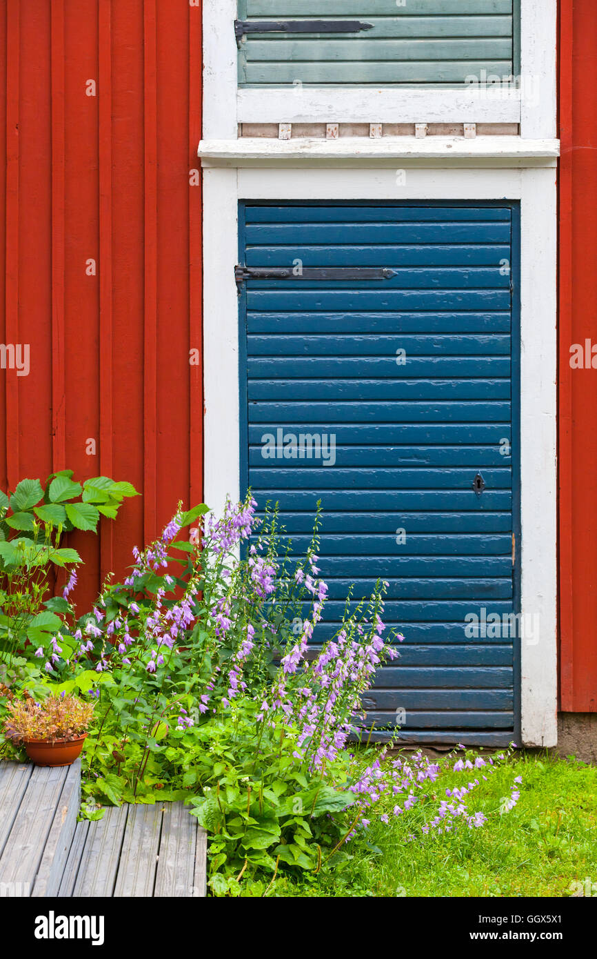 Porvoo, Finnland. Alte traditionelle finnische Architektur-Fragment. Dekorative Blumen in der Nähe von rote blaue Tür im roten Holzwand Stockfoto
