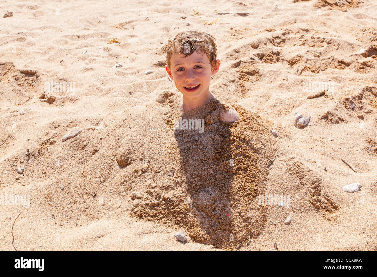 Sechs Jahre alter Junge vergraben im Sand, Hope Cove, Devon, England, Vereinigtes Königreich Stockfoto