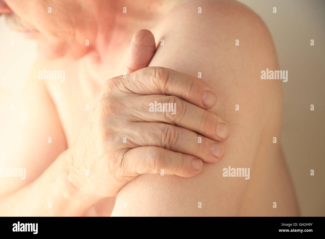 Ein älterer Mann mit seiner Hand auf einer Fläche von Schmerzen auf seinem Oberarm Stockfoto