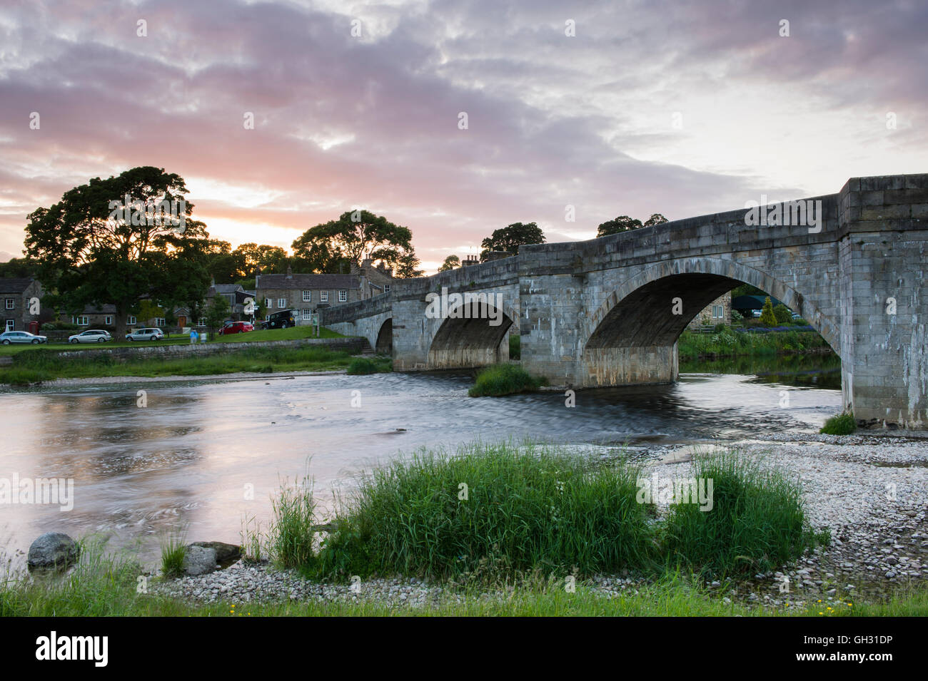 Steinerne Brücke über dem Fluss Wharfe, fließt sie durch eine malerische Burnsall Dorf, unter dramatischen Sommer Abend Red Sky - Yorkshire Dales, England, UK. Stockfoto