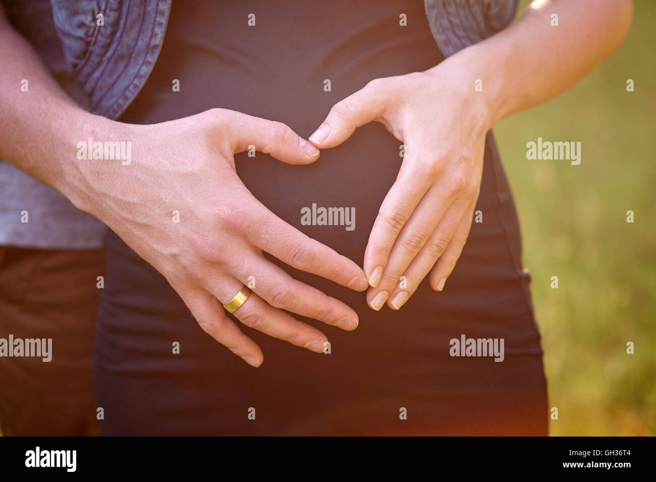Schwangeren Bauch mit den Fingern des Mannes Herz-symbol Stockfoto