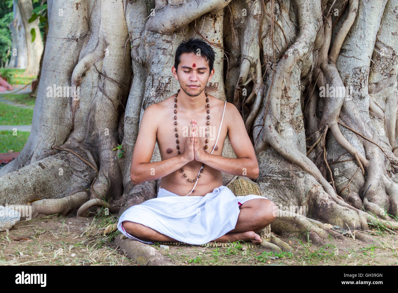 Ein junger Hindu Mann sitzt in der Meditation unter einem Banyanbaum. Stockfoto