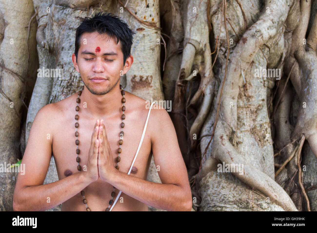 Ein junger Hindu Mann sitzt in der Meditation unter einem Banyanbaum. Stockfoto