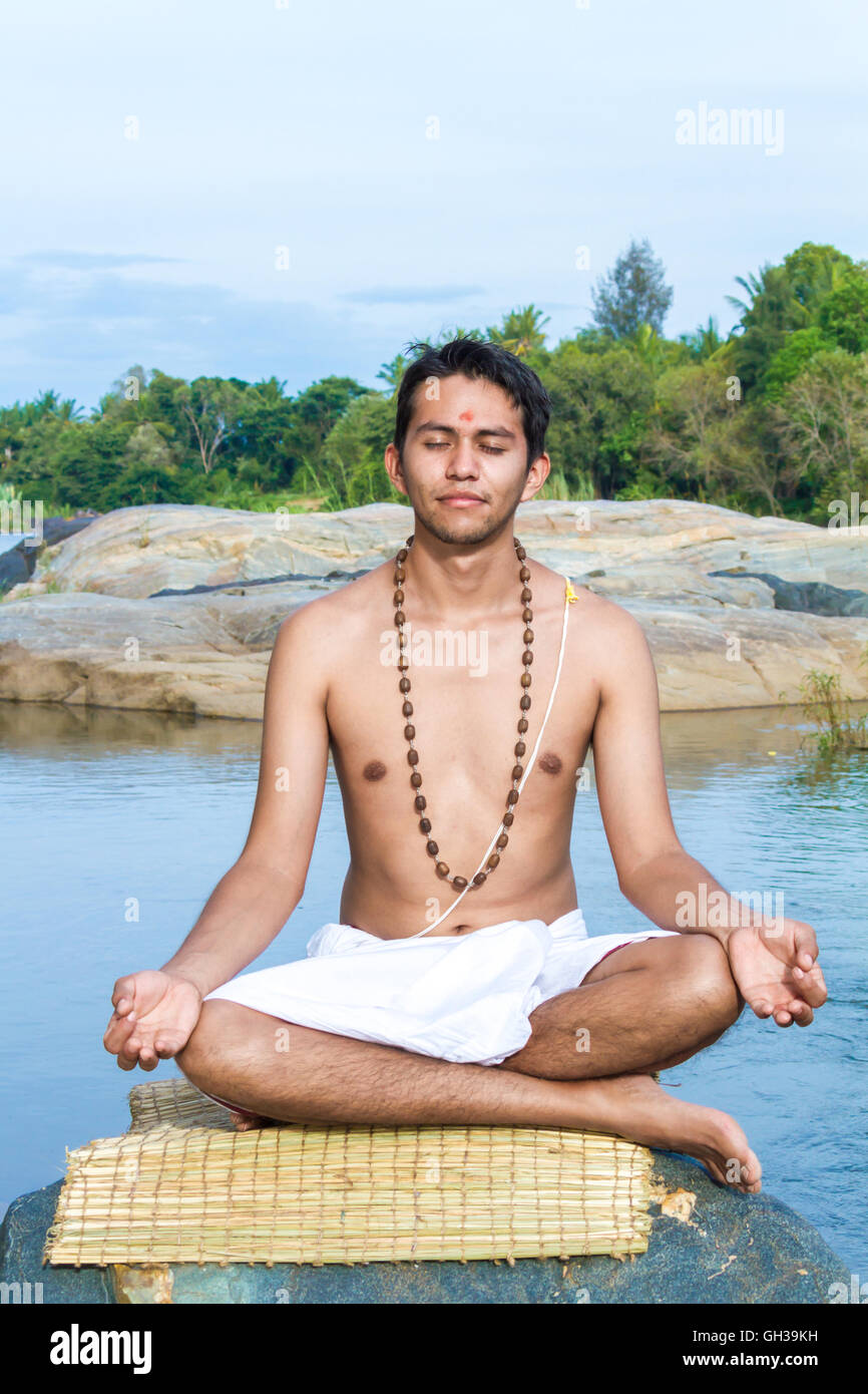 Ein junger Hindu Priester (Brahmanen), sitzt in der Meditation am Ufer eines Flusses. Stockfoto