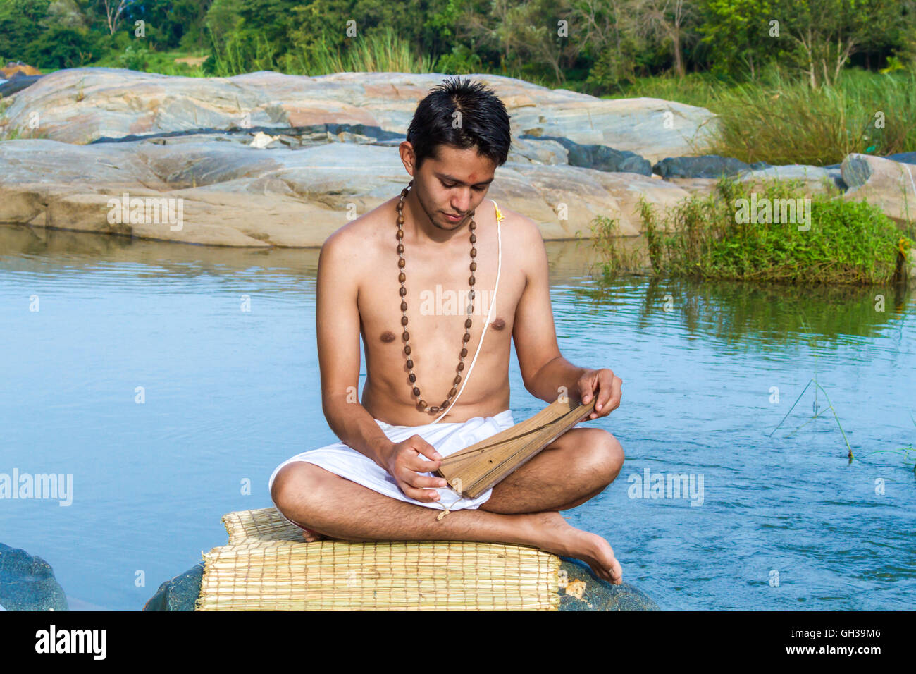 Ein junger Brahmane liest eine alte Hindu Palmblatt Schrift an einem Flussufer. Stockfoto