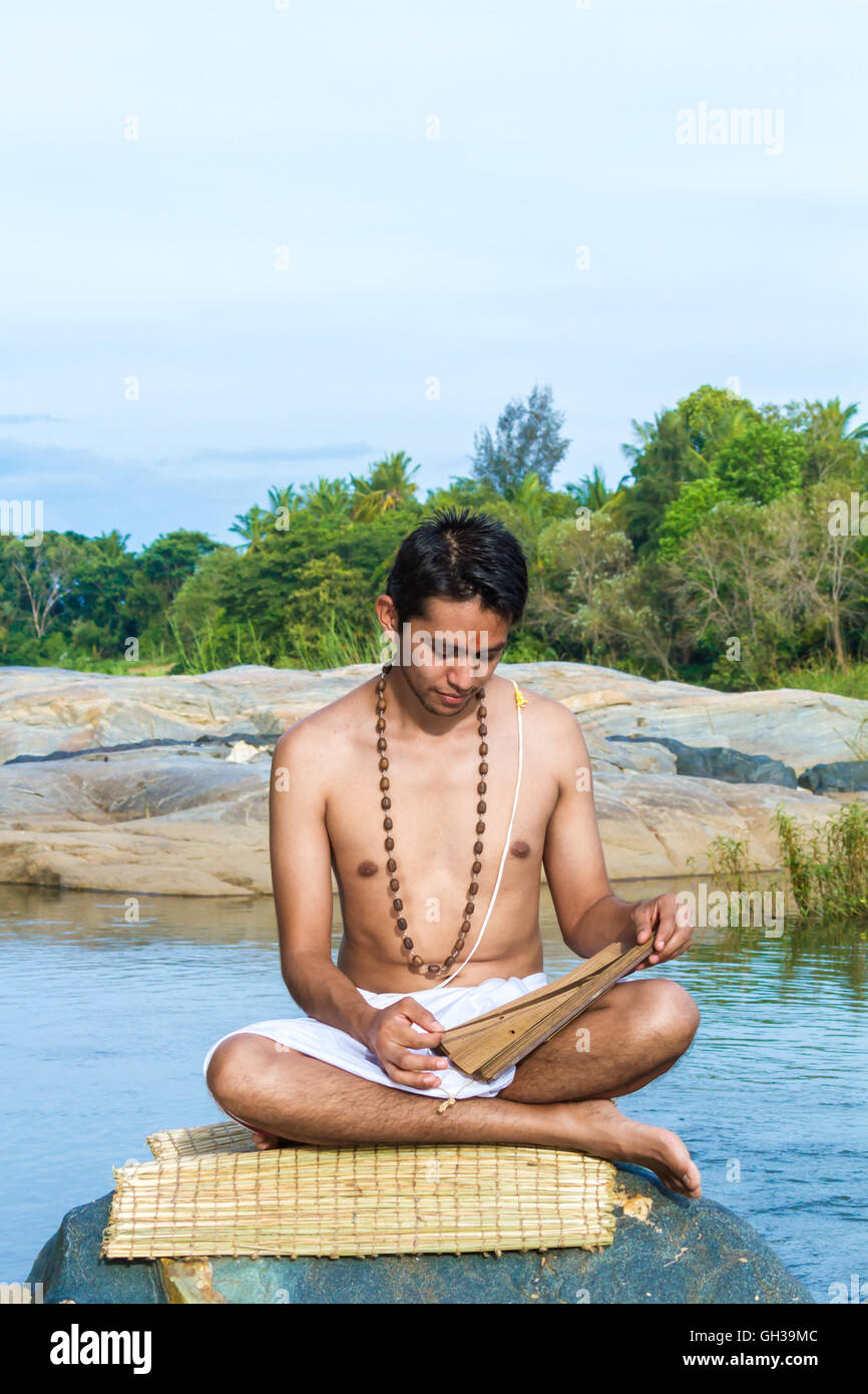 Ein junger Brahmane liest eine alte Hindu Palmblatt Schrift an einem Flussufer. Stockfoto