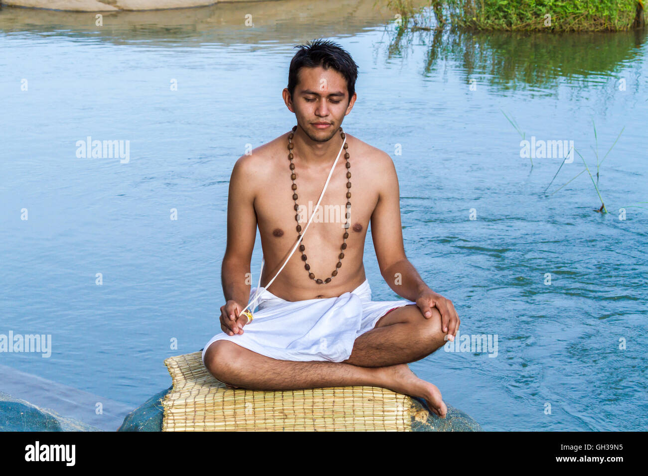 Ein junger Hindu Priester (Brahmanen) sitzt in der Meditation am Ufer eines Flusses. Stockfoto