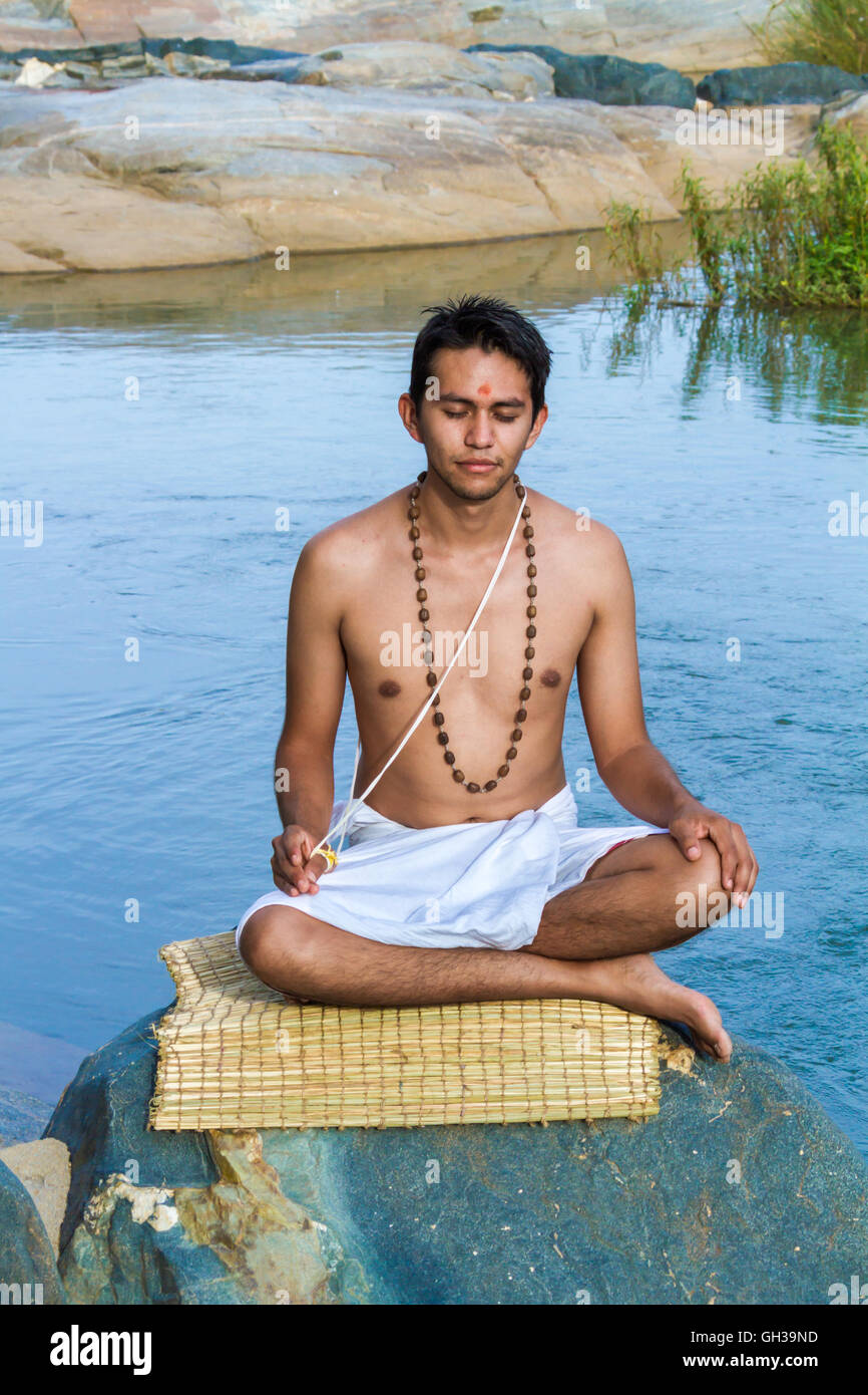 Ein junger Hindu Priester (Brahmanen) sitzt in der Meditation am Ufer eines Flusses. Stockfoto