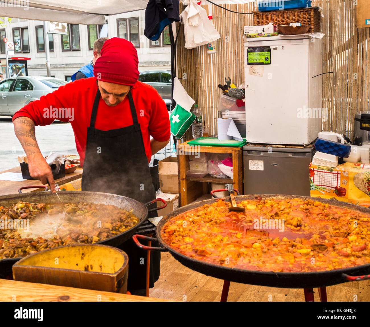 Ein Stallhalter kocht und stiert große Tabletts mit heißem, dampfendem gelbem Curry, die in einem Stall am Southbank Center Food Market, London SE1, gekocht werden Stockfoto