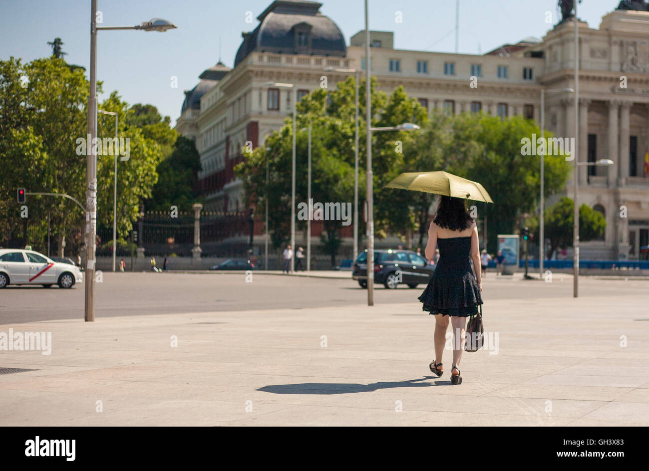 Junge Frau, die zu Fuß durch Madrid Stadtstraßen mit Regenschirm ein heißer Sommertag Stockfoto