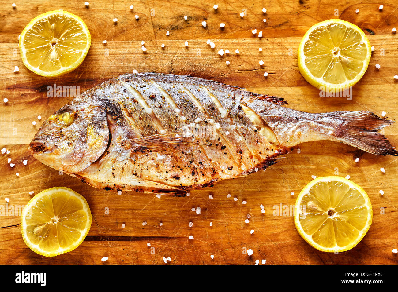 Vergoldete Kopf Brassen Fisch auf einem Holztisch mit Zitronen und Meersalz gekörnt geröstet. Stockfoto