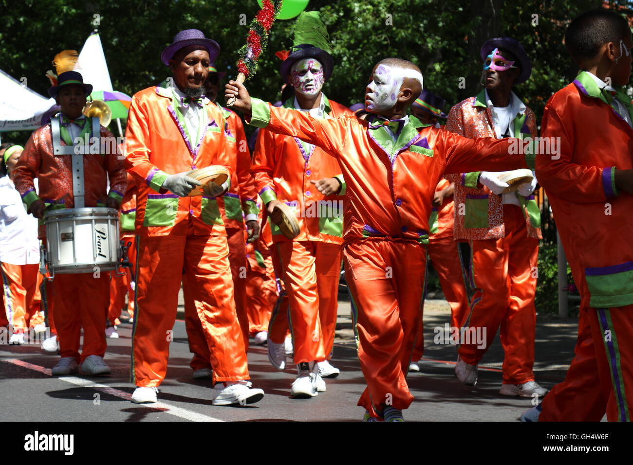 Afrikanische Männer in orange Outfits und Gesichter bemalt bei der 2016 Stellenbosch Wein-Parade Musizieren mit Trommeln und Tamburins Stockfoto
