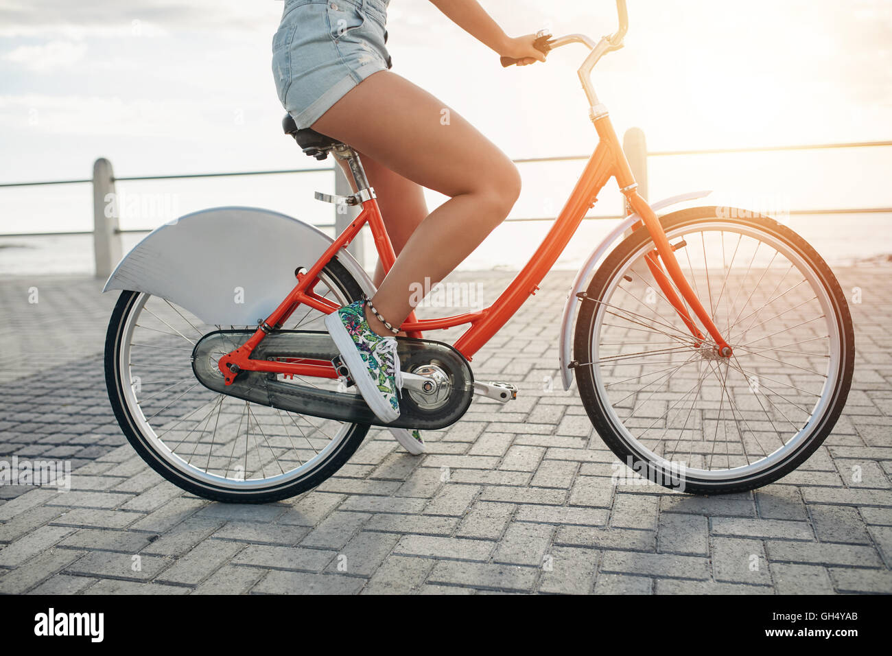 Niedrige Abschnitt Schuss der jungen Frau auf ihrem Fahrrad auf der Küstenstraße. Weibliche Radfahrer auf Promenade an einem sonnigen Tag. Stockfoto