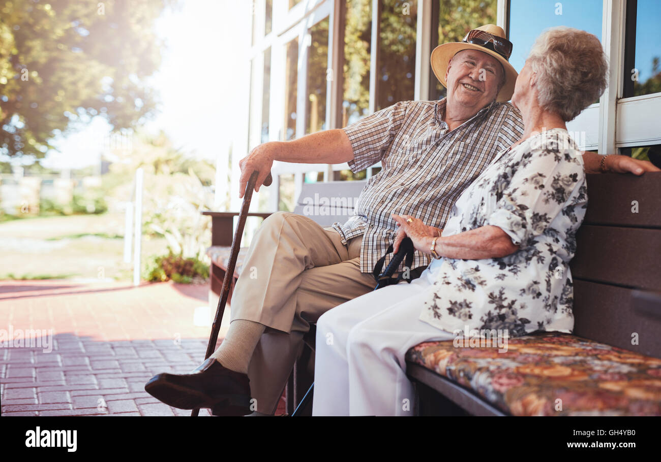 Älteres Paar mit einem Chat beim Sitzen auf einer Bank außerhalb der eigenen Wohnung zu lieben. Gerne älteres Paar auf Bank gemeinsam entspannen. Stockfoto