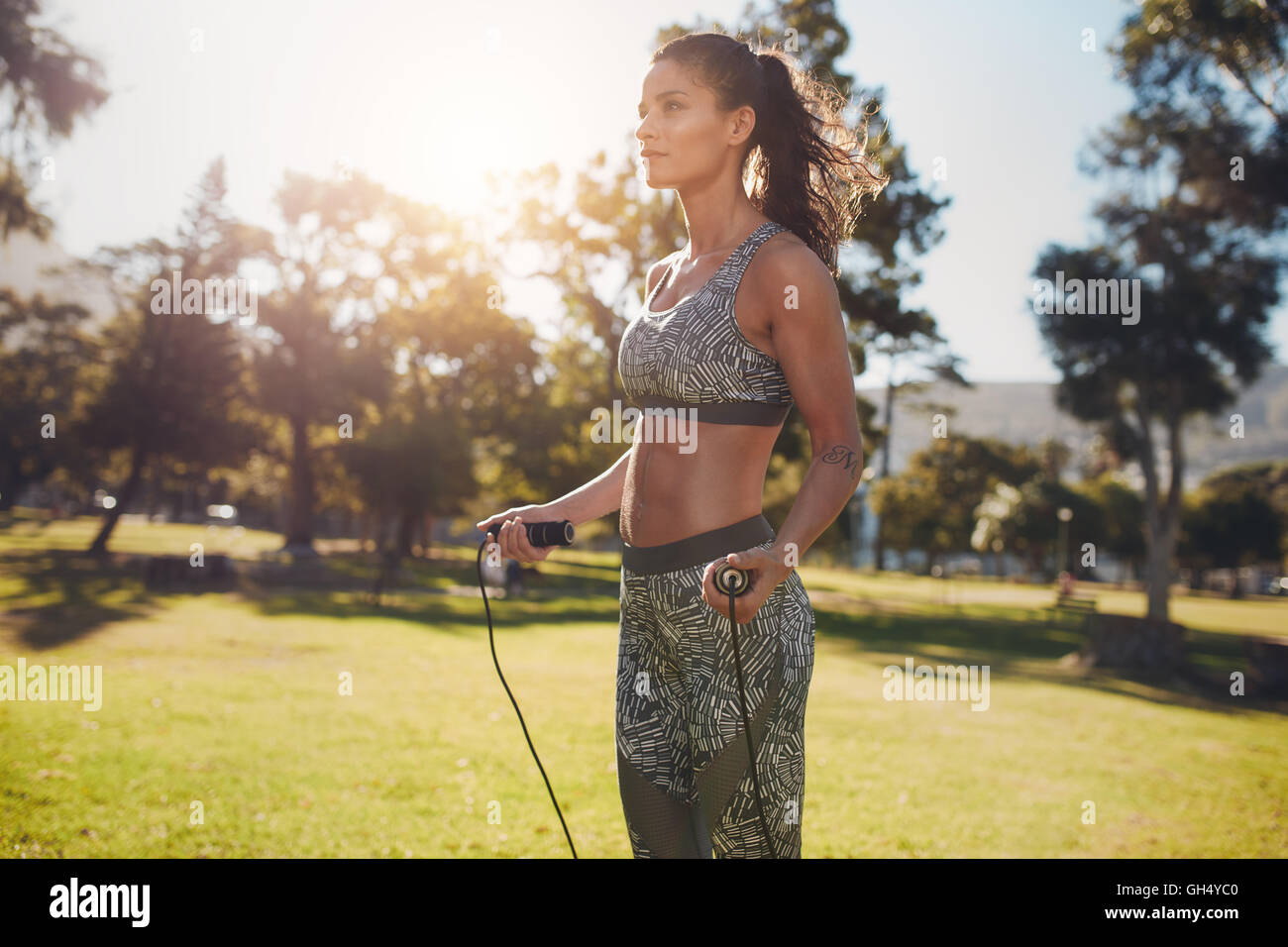 Außenaufnahme einer entschlossenen Frau, die draußen in der Natur springt. Fitness-Frau, die an einem sonnigen Tag mit Sprungseil in einem Park trainiert. Stockfoto