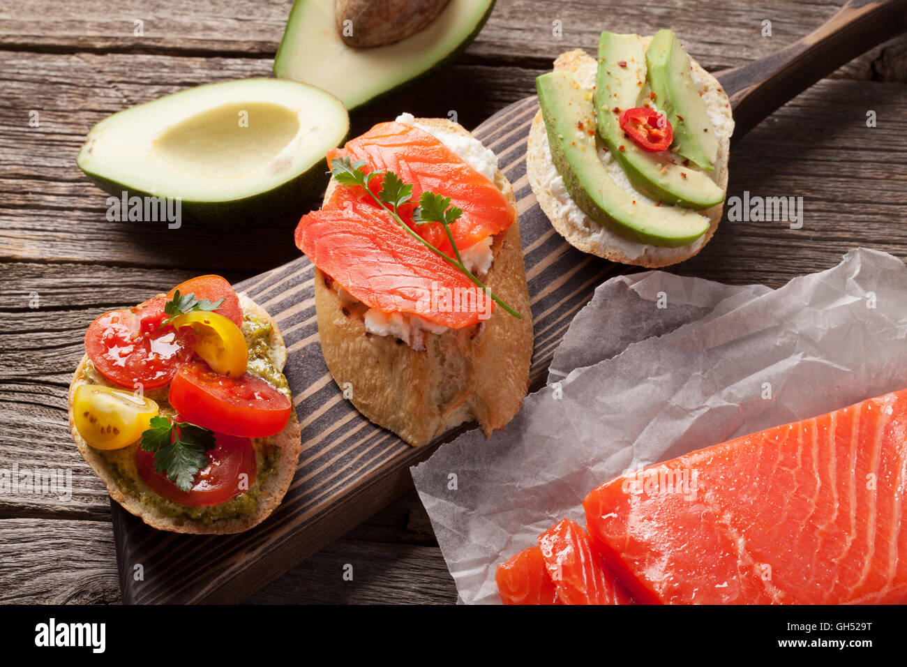 Toast-Sandwiches mit Avocado, Tomaten und Lachs auf hölzernen Hintergrund Stockfoto