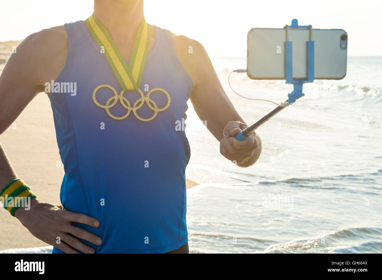 RIO DE JANEIRO - 10. März 2016: Sportler mit Olympischen Ringen Goldmedaille steht unter einem Selfie am Sonnenaufgang Strand. Stockfoto