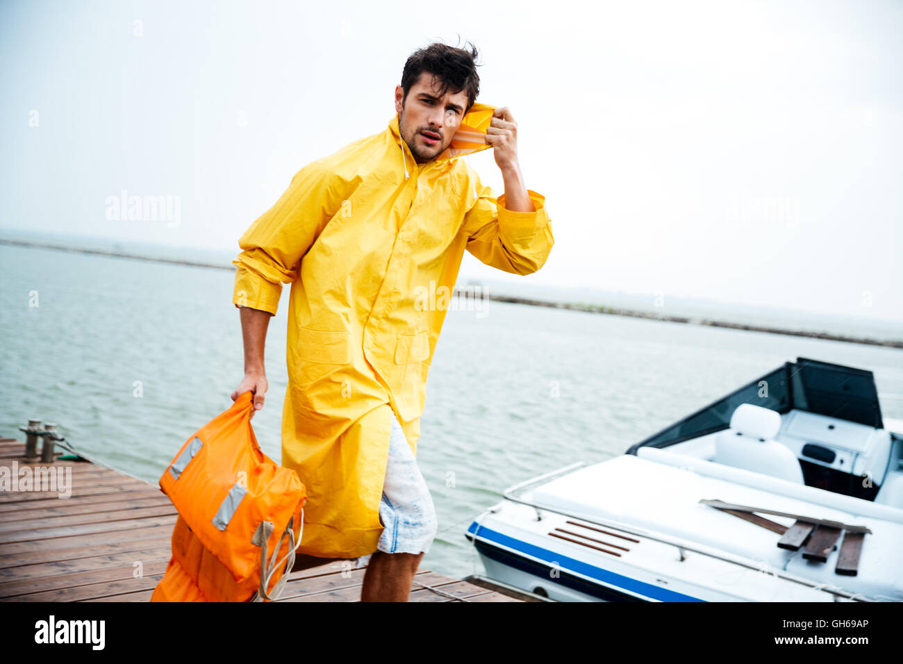 Junge hübsche Seemann Mann in gelben Mantel zu Fuß am Meer Pier holding  Schwimmweste Stockfotografie - Alamy