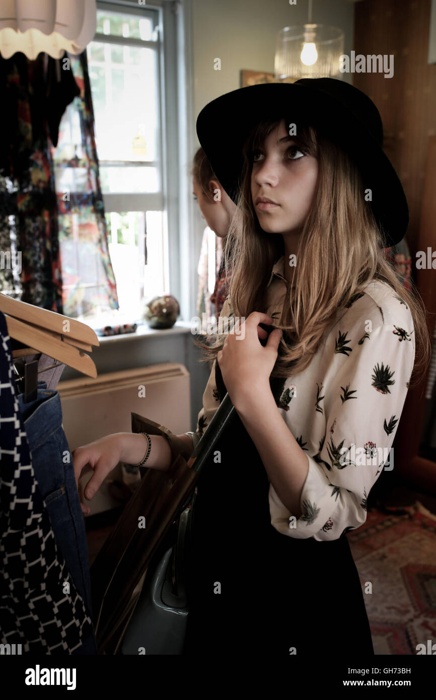 12 Jahre altes Mädchen trägt einen schwarzen Hut in einem Vintage-Kleidung-Shop surfen, Blick nach oben in Richtung Kleidung. Mädchen hat dunkel blonde Haare Stockfoto