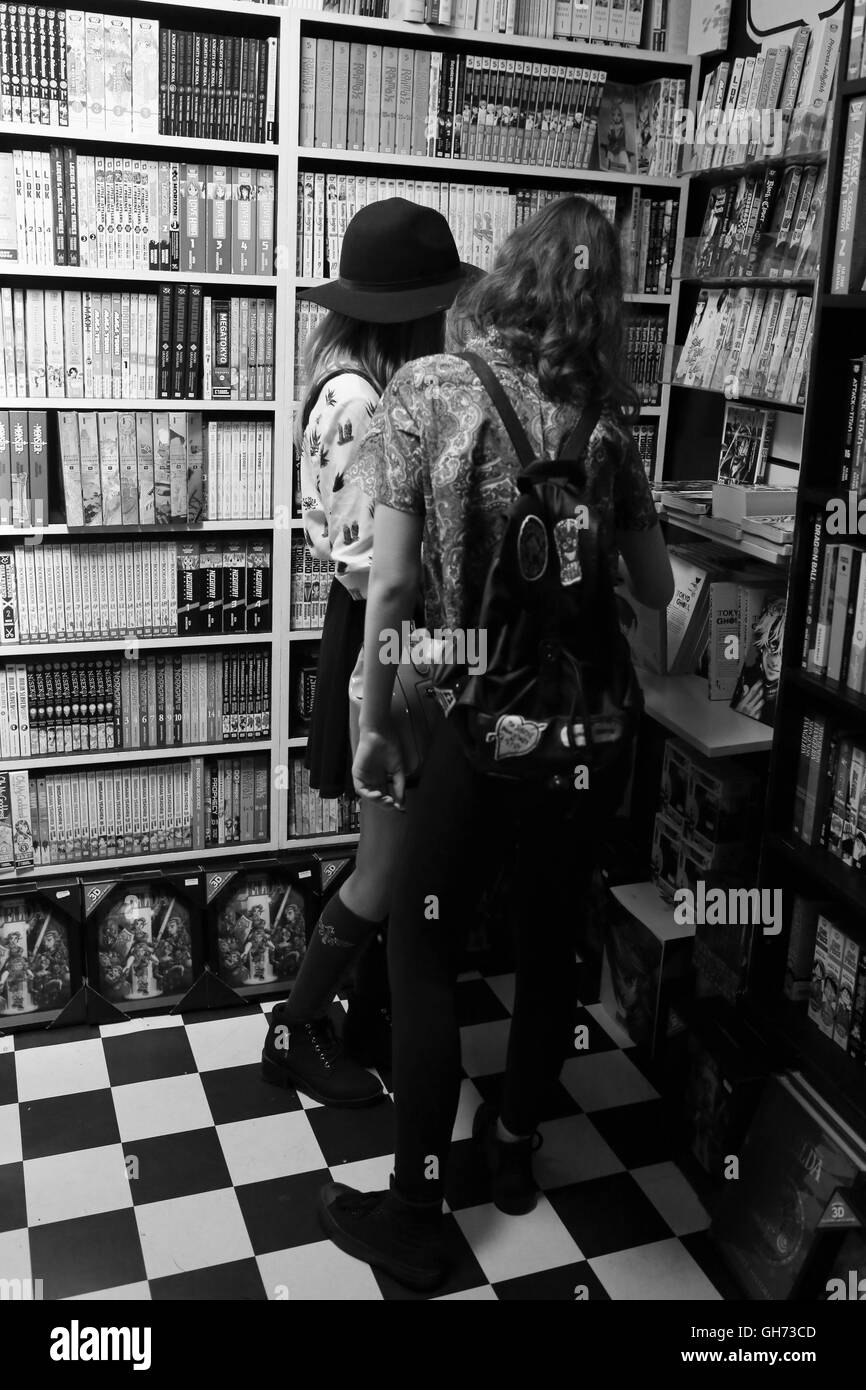 Zwei Jugendliche Bücher in einem Buchladen, umgeben von Regalen Boden bis zur Decke gefüllt mit Büchern anschauen. Stockfoto